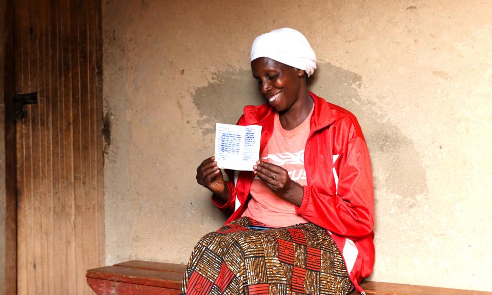 Inside her house, Agnes proudly shows the VSLA record book, smiling as she points to the long list of loans, repayments, and savings registered in it. Photo: UN Women/Silvia Lanzarini