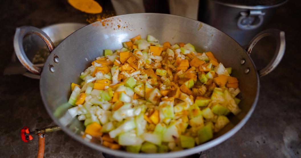 Assorted chopped vegetables being cooked in a large metal pan.
