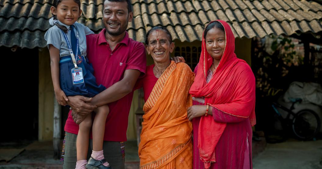 Nirmala is standing with her family, smiling and looking at the camera.